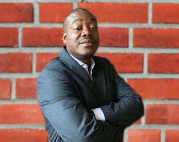 Headshot of Yves De Souza in front of a red-brick wall