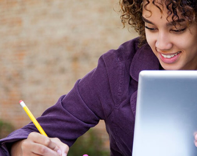 Black student learning on an tablet while taking notes on a notpad