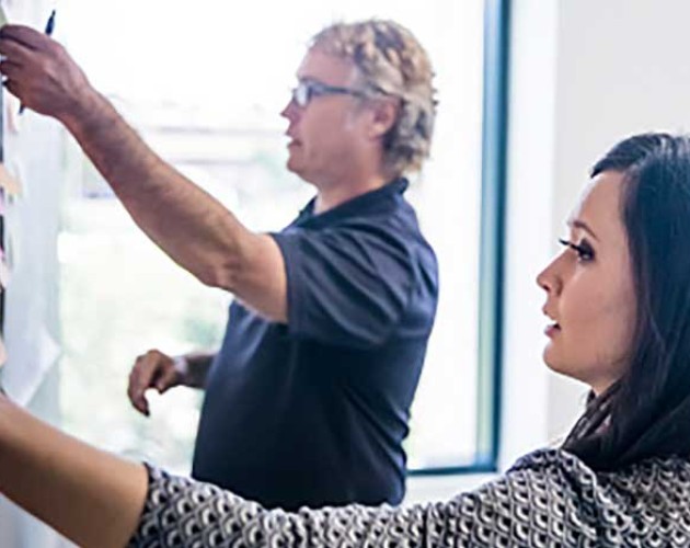 Photo of man and woman putting post-it notes on a blackboard