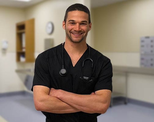 Alexander Lipson in his nursing outfit standing in front of a clinical setting