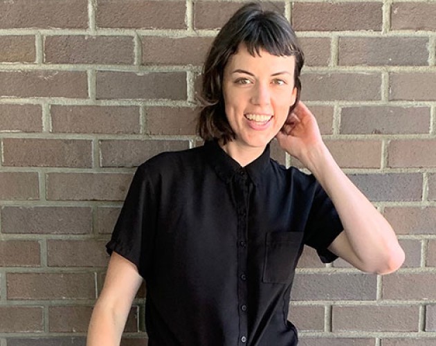 Professional Sequence in Editing gradaute Alison Kranz standing in front of a brick wall, hand brushing back hair by ear