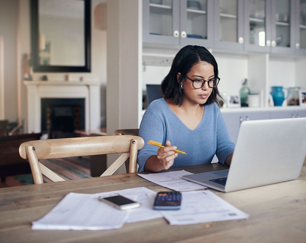 Woman sitting at kitchen table looking at laptop working on financial reports