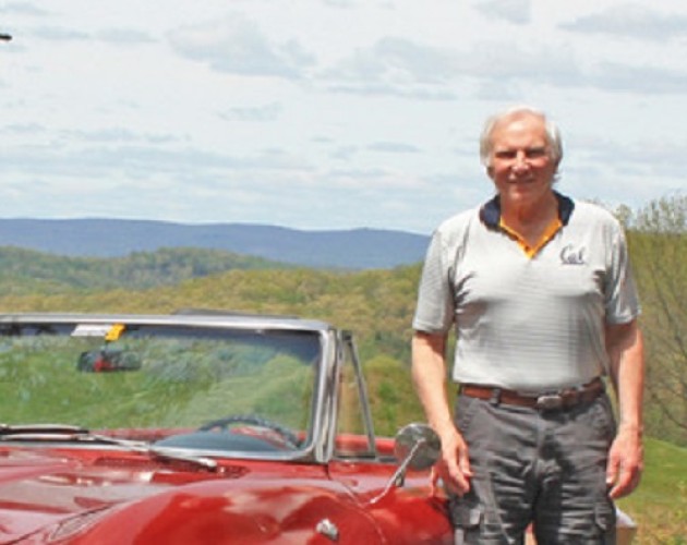 Writing certificate graduate and author Bill Truran next to a red sports car with hills behind him. Photo.