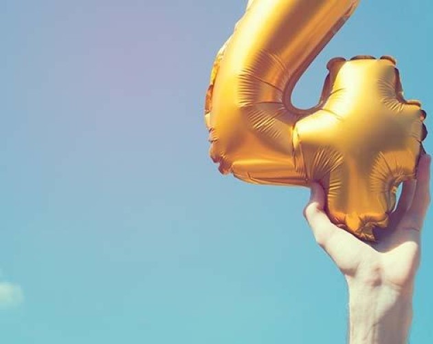 Image of hand holding a number 4 balloon against a blue sky