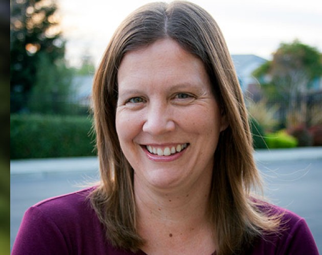 Headshot of Editing Honored Instructor Cathleen Small, standing outside with a neighborhood and sunset in background