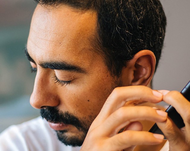 Photo of man eyes closed, turned away from cell phone, listening with left ear