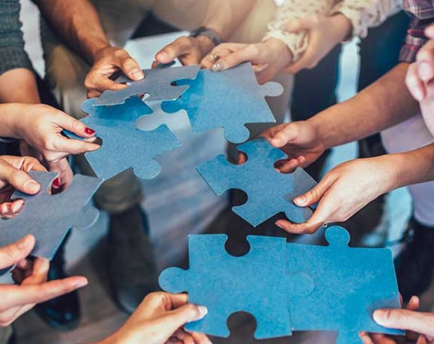 Multicultural employees putting together oversized jigsaw puzzle pieces