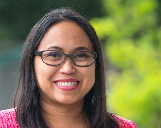 Project Management graduate Hazel Johanson, wearing glasses and smiling, outside with a green leafy background