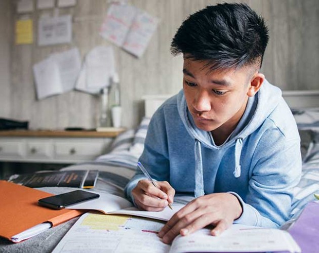 Photo of student lying on bed doing homework