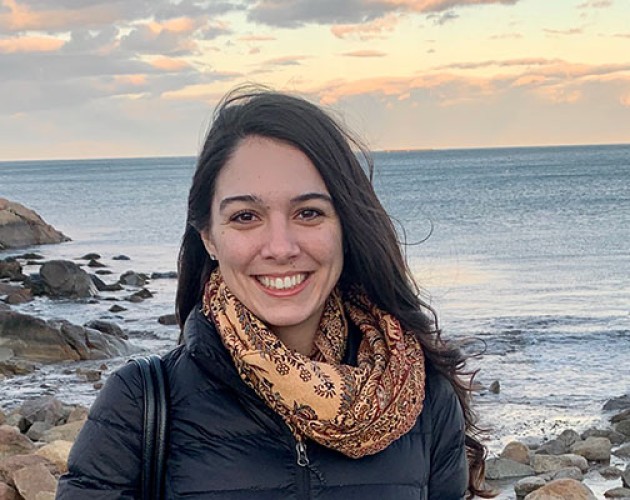 Photo of Post-Bacc Counseling and Psychology program graduate Lisell Perez-Rogers standing on an oceanfront with sunset and rocks in background