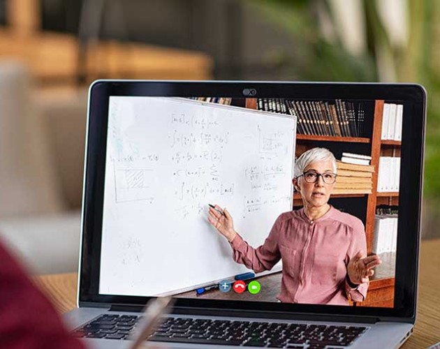 Photo of student looking at a laptop screen with instructor teaching on a whiteboard