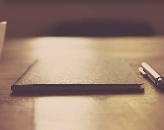 Image of closed notebook and pen on wooden table