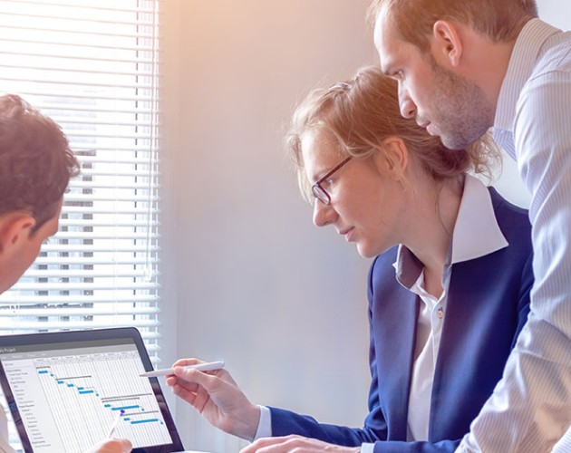 Three staff members gather around a laptop computer looking at a project chart