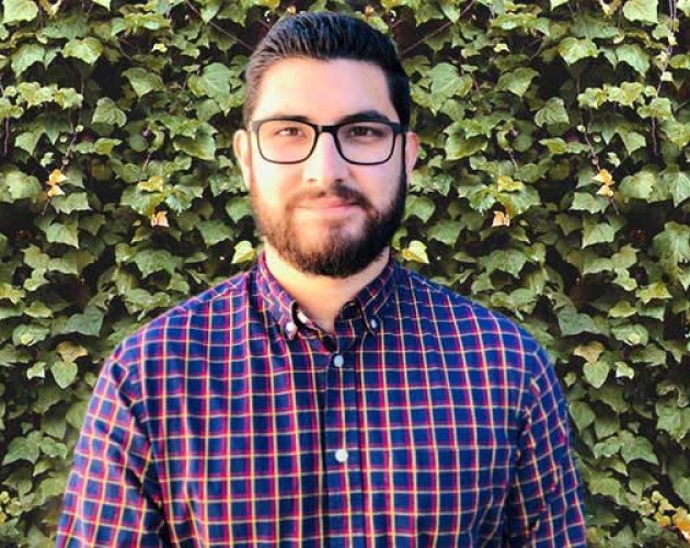 Graduate Raul Acosta stands in front of a wall covered in ivy