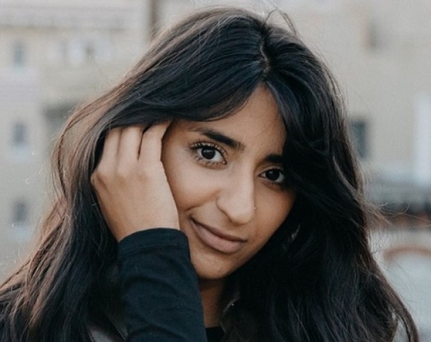 UX Design graduate Sana Maqsood outside with hand behind ear, in long dark hair. Photo.