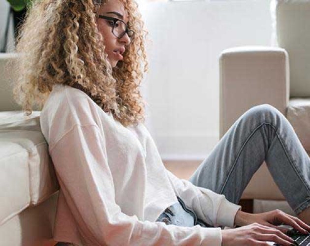 Black woman sitting on the floor typing on a laptop