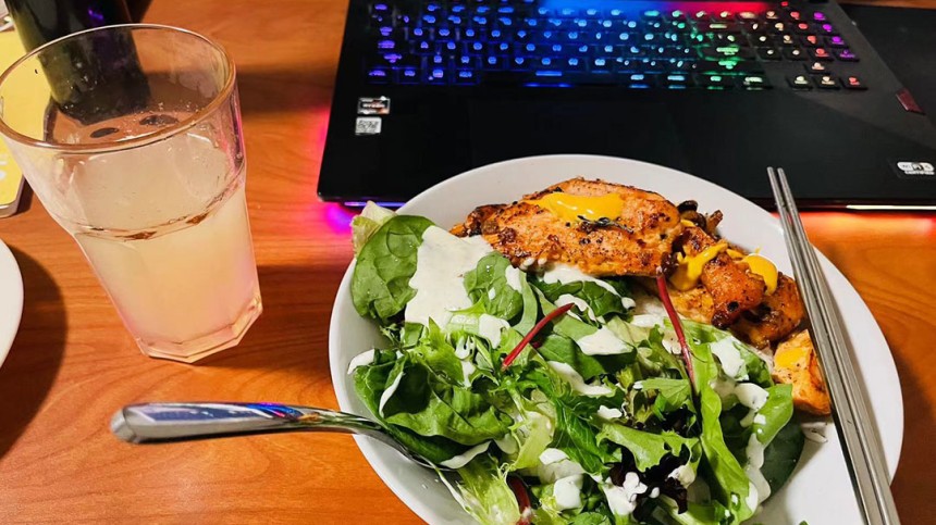 Photo of a salad and a glass of water in front of a laptop